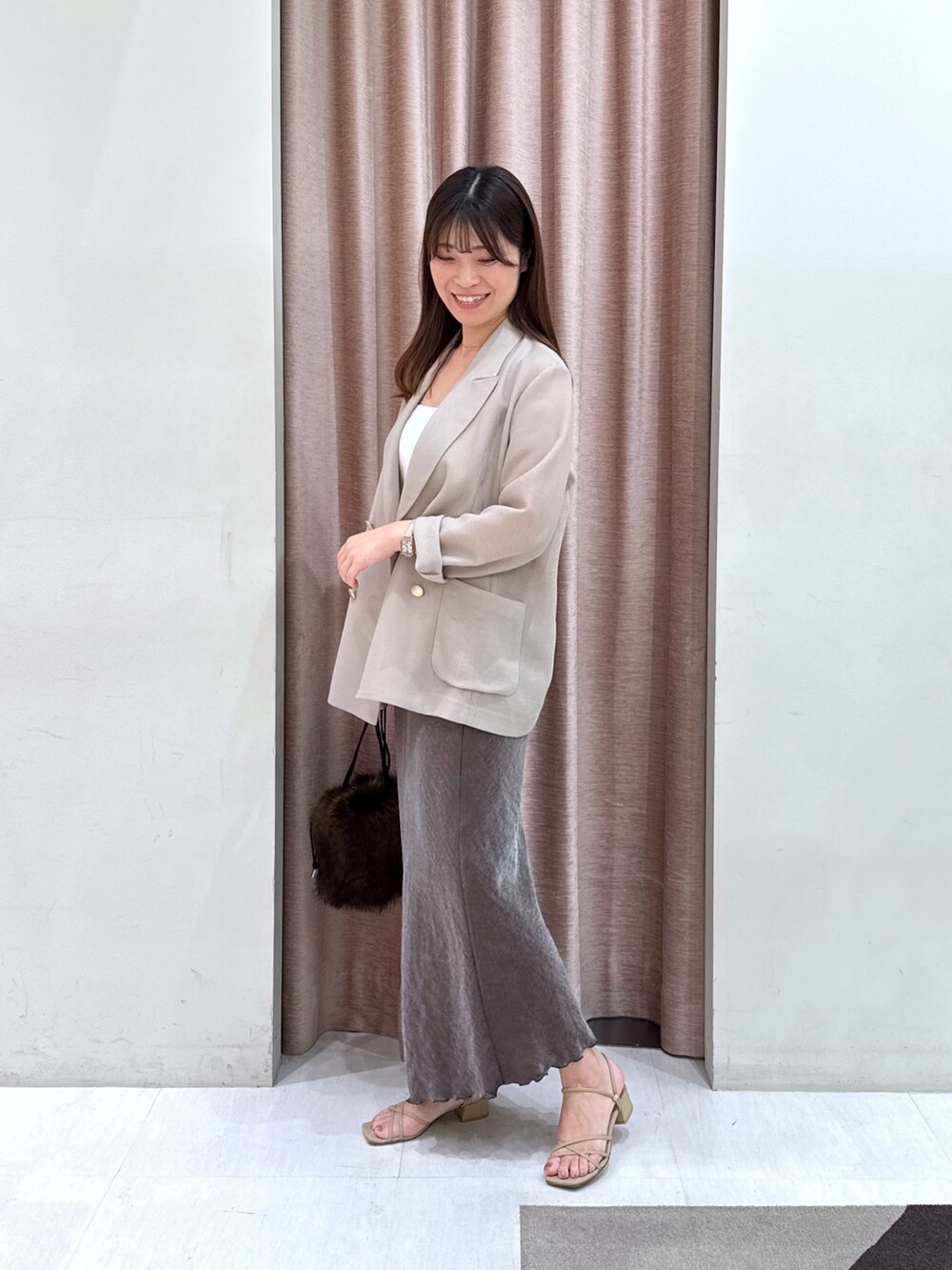 ベージュ系のテーラードジャケット、ホワイト系のキャミソール、ブラウン系のスカートを着用したレディースの秋コーディネートの2枚目の写真