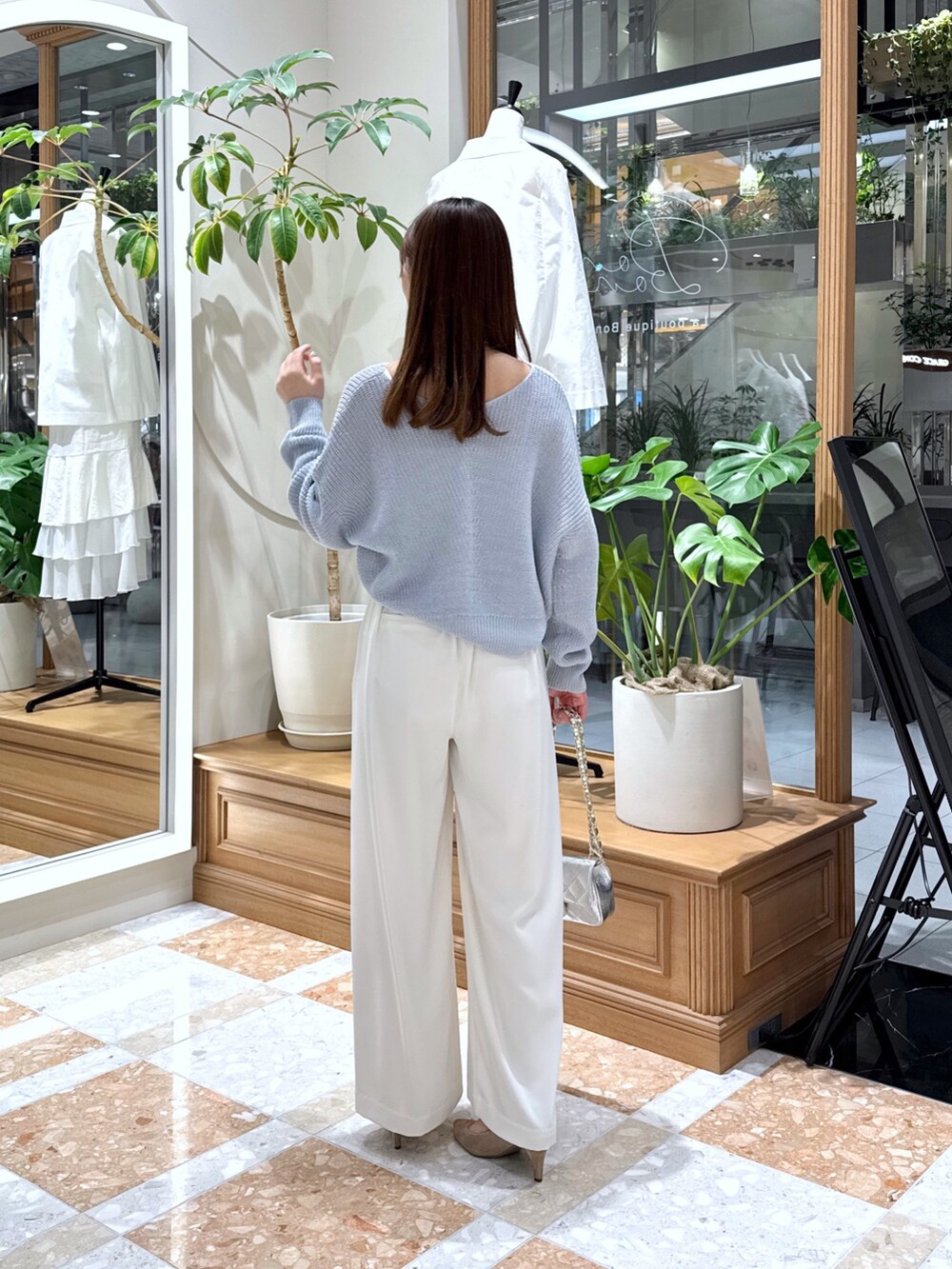 シルバー系のハンドバッグ、ホワイト系のスラックス、ブルー系のニット/セーターを着用したレディースの春コーディネートの2枚目の写真