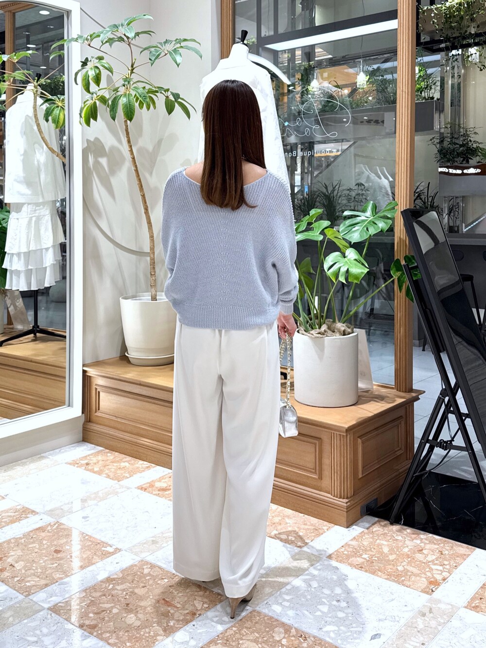 シルバー系のハンドバッグ、ホワイト系のスラックス、ブルー系のニット/セーターを着用したレディースの春コーディネートの3枚目の写真