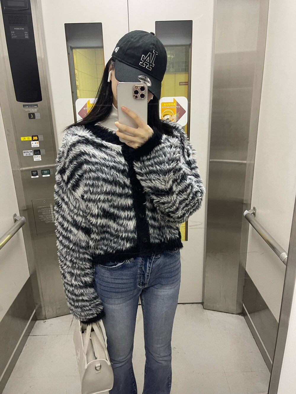 ブラック系のカーディガン/ボレロ、ホワイト系のハンドバッグ、ブルー系のデニムパンツを着用したレディースの秋コーディネートの2枚目の写真