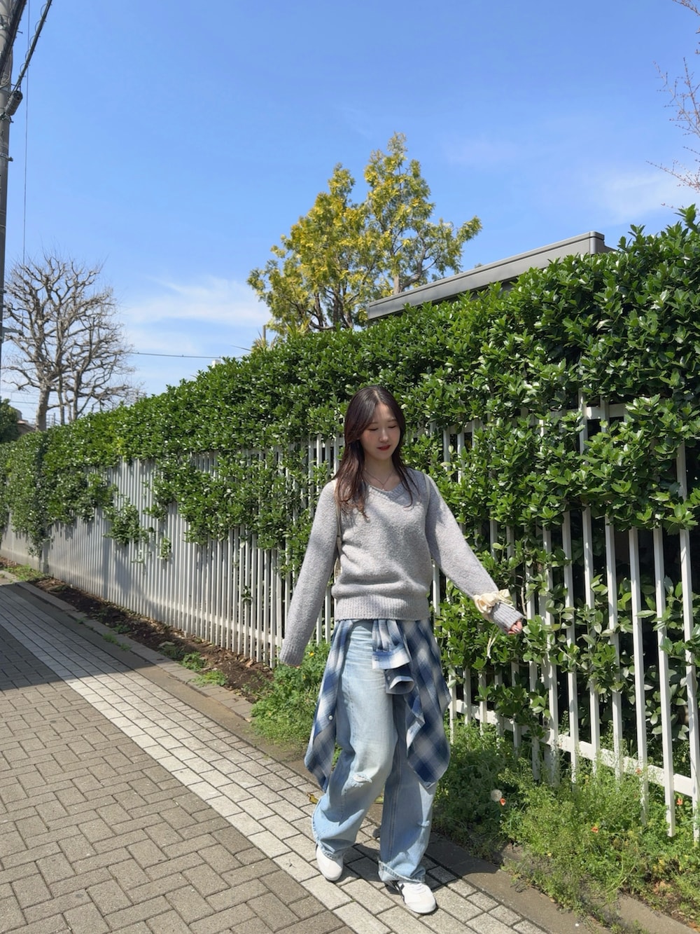 グレー系のニット/セーター、ブルー系のシャツ/ブラウス、ブルー系のデニムパンツを着用したレディースの春コーディネートの2枚目の写真