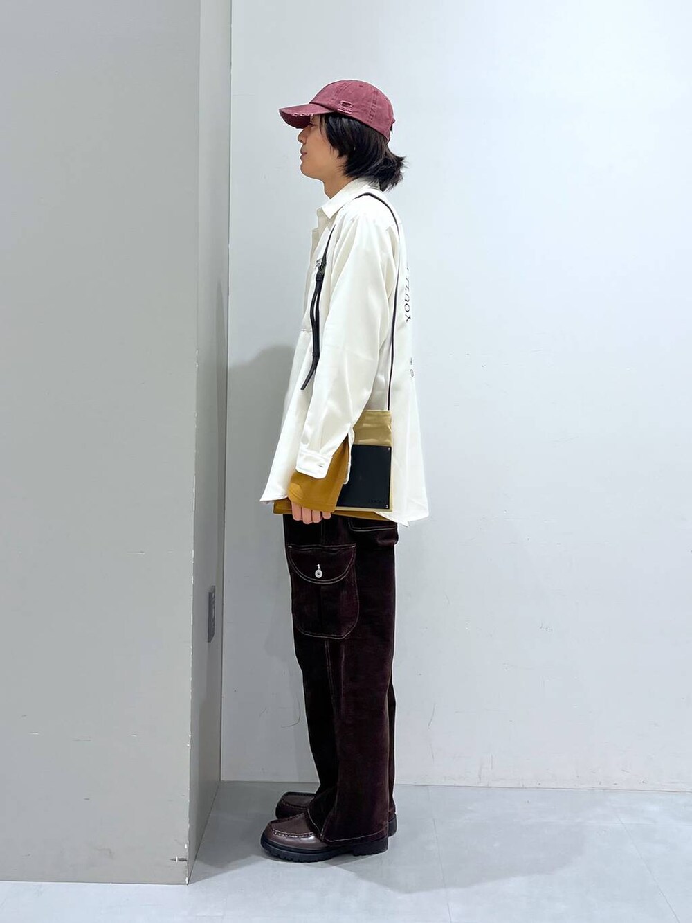 イエロー系のTシャツ/カットソー、ブラウン系のその他パンツ、ベージュ系のショルダーバッグを着用したメンズの冬コーディネートの2枚目の写真