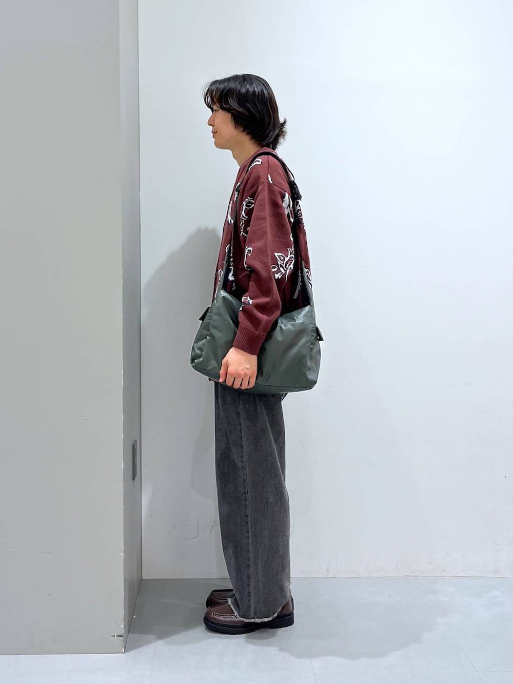 グリーン系のショルダーバッグ、グレー系のデニムパンツ、ブラウン系のローファーを着用したメンズの秋コーディネートの2枚目の写真