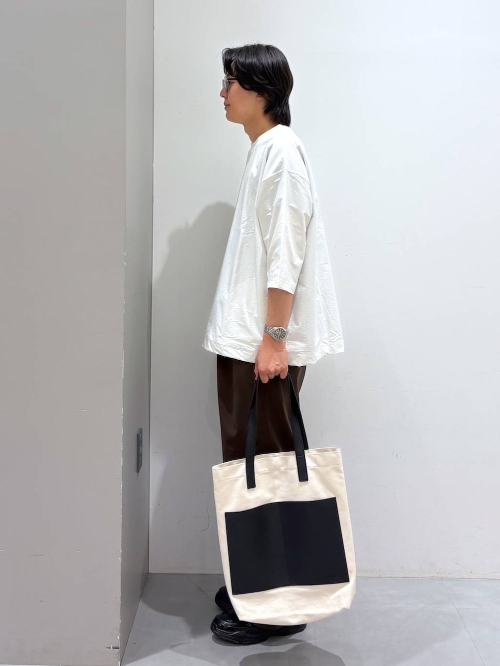 ベージュ系のトートバッグ、ブラウン系のその他パンツ、ホワイト系のTシャツ/カットソーを着用したメンズの夏コーディネートの2枚目の写真