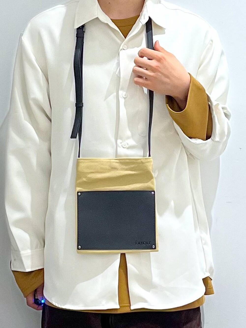 イエロー系のTシャツ/カットソー、ブラウン系のその他パンツ、ベージュ系のショルダーバッグを着用したメンズの冬コーディネートの4枚目の写真