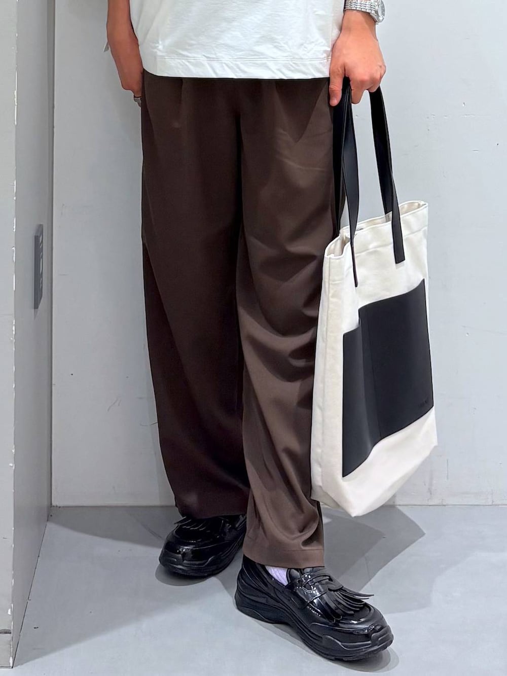 ベージュ系のトートバッグ、ブラウン系のその他パンツ、ホワイト系のTシャツ/カットソーを着用したメンズの夏コーディネートの4枚目の写真