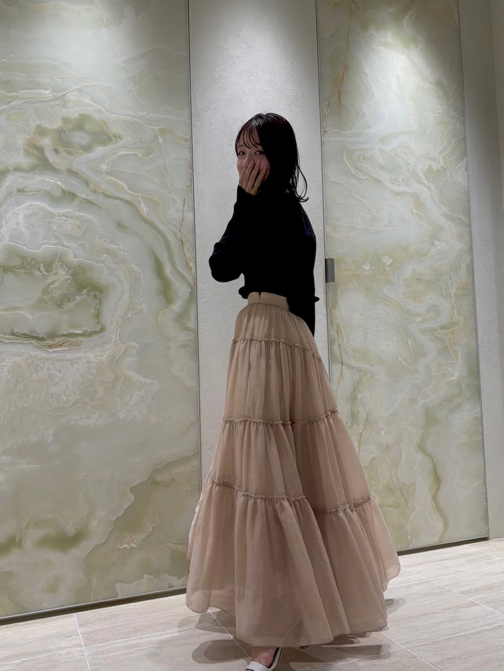 ブラック系のカーディガン/ボレロ、ベージュ系のスカート、ホワイト系のサンダルを着用したレディースの春コーディネートの2枚目の写真