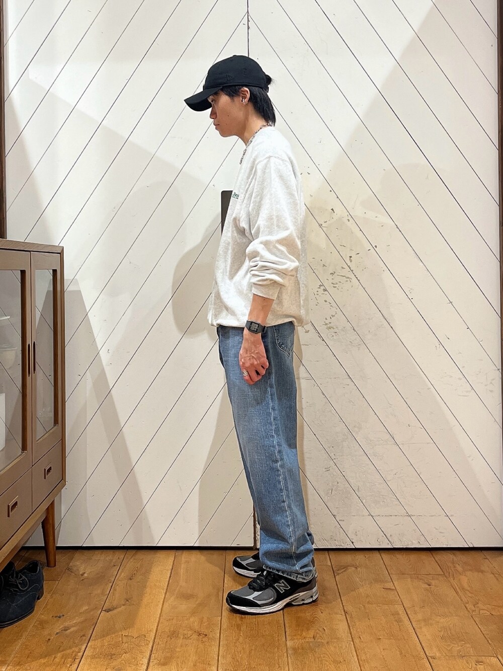 グレー系のスウェット、ブルー系のデニムパンツ、ブラック系のスニーカーを着用したメンズの秋コーディネートの2枚目の写真