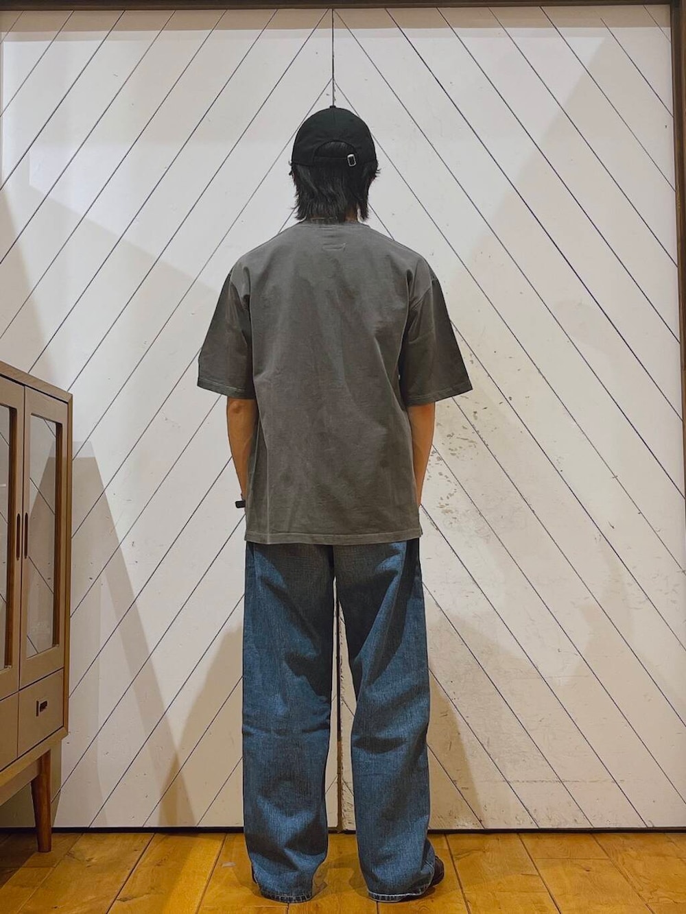 ブルー系のデニムパンツ、グレー系のTシャツ/カットソー、ブラック系のキャップを着用したメンズの夏コーディネートの2枚目の写真