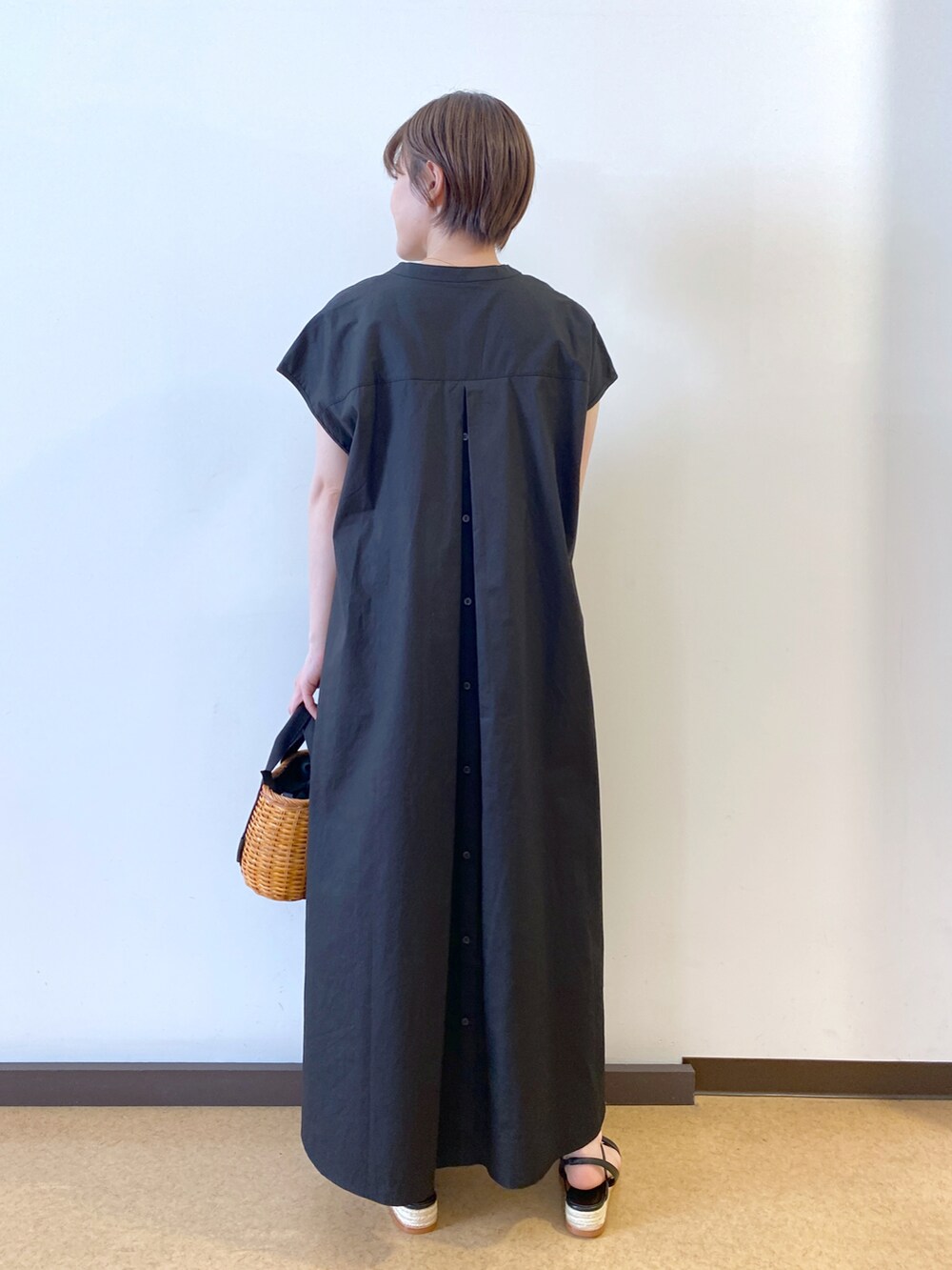 イエロー系のかごバッグ、ブラック系のワンピース、ブラック系のサンダルを着用したレディースの春コーディネートの2枚目の写真