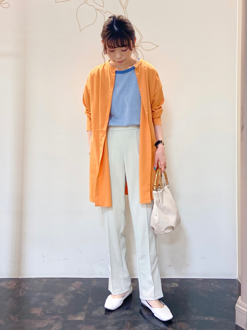 オレンジ系のシャツ/ブラウス、ブルー系のTシャツ/カットソー、ホワイト系のスラックスを着用したレディースの春コーディネートの2枚目の写真