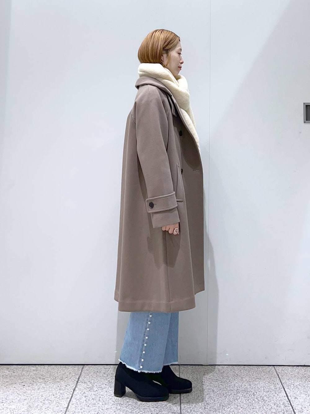 ホワイト系のニット/セーター、ブラウン系のチェスターコート、ブラック系のブーツを着用したレディースの冬コーディネートの2枚目の写真