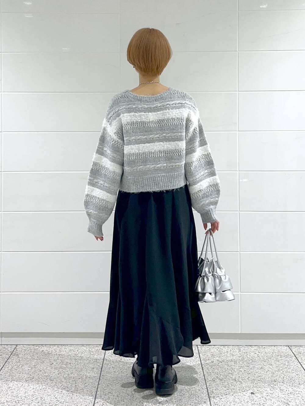 シルバー系のショルダーバッグ、ブラック系のブーツ、ブラック系のスカートを着用したレディースの冬コーディネートの3枚目の写真