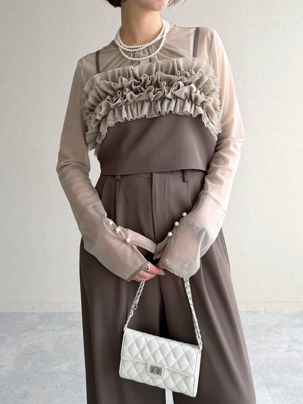 ブラック系のパンプス、ホワイト系のショルダーバッグ、ベージュ系のパンツドレスを着用したレディースの春コーディネートの5枚目の写真