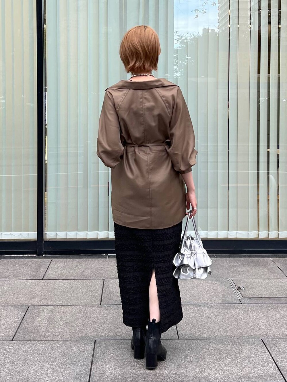 シルバー系のショルダーバッグ、ブラック系のブーツ、ブラック系のスカートを着用したレディースの秋コーディネートの2枚目の写真