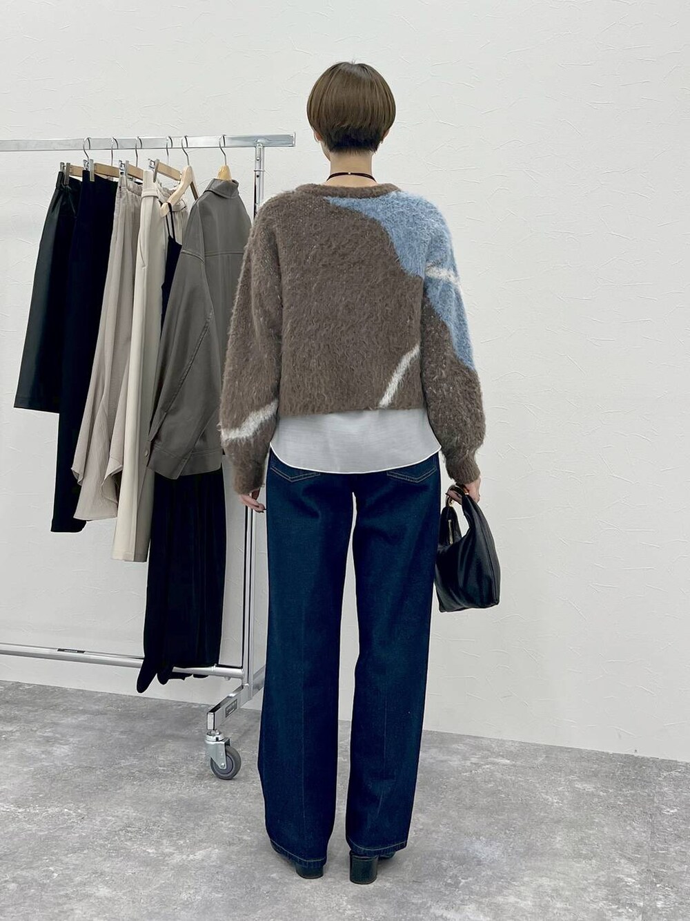ブラウン系のニット/セーター、ブラック系のハンドバッグ、ブルー系のデニムパンツを着用したレディースの秋コーディネートの4枚目の写真