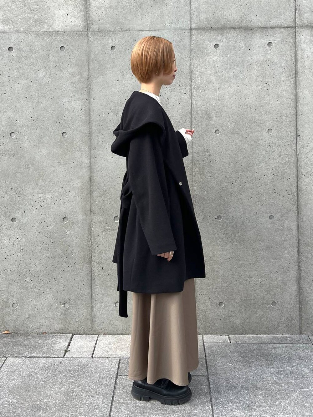 ブラック系のノーカラーコート、ブラック系のブーツ、ホワイト系のショルダーバッグを着用したレディースの冬コーディネートの2枚目の写真