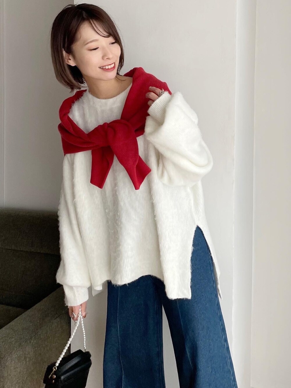 レッド系のカーディガン/ボレロ、ホワイト系のニット/セーター、ブルー系のデニムパンツを着用したレディースの冬コーディネートの4枚目の写真