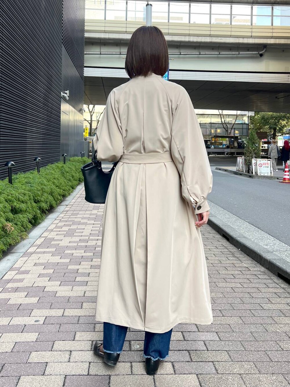 ブラック系のハンドバッグ、ブラック系のパンプス、ベージュ系のトレンチコートを着用したレディースの春コーディネートの2枚目の写真