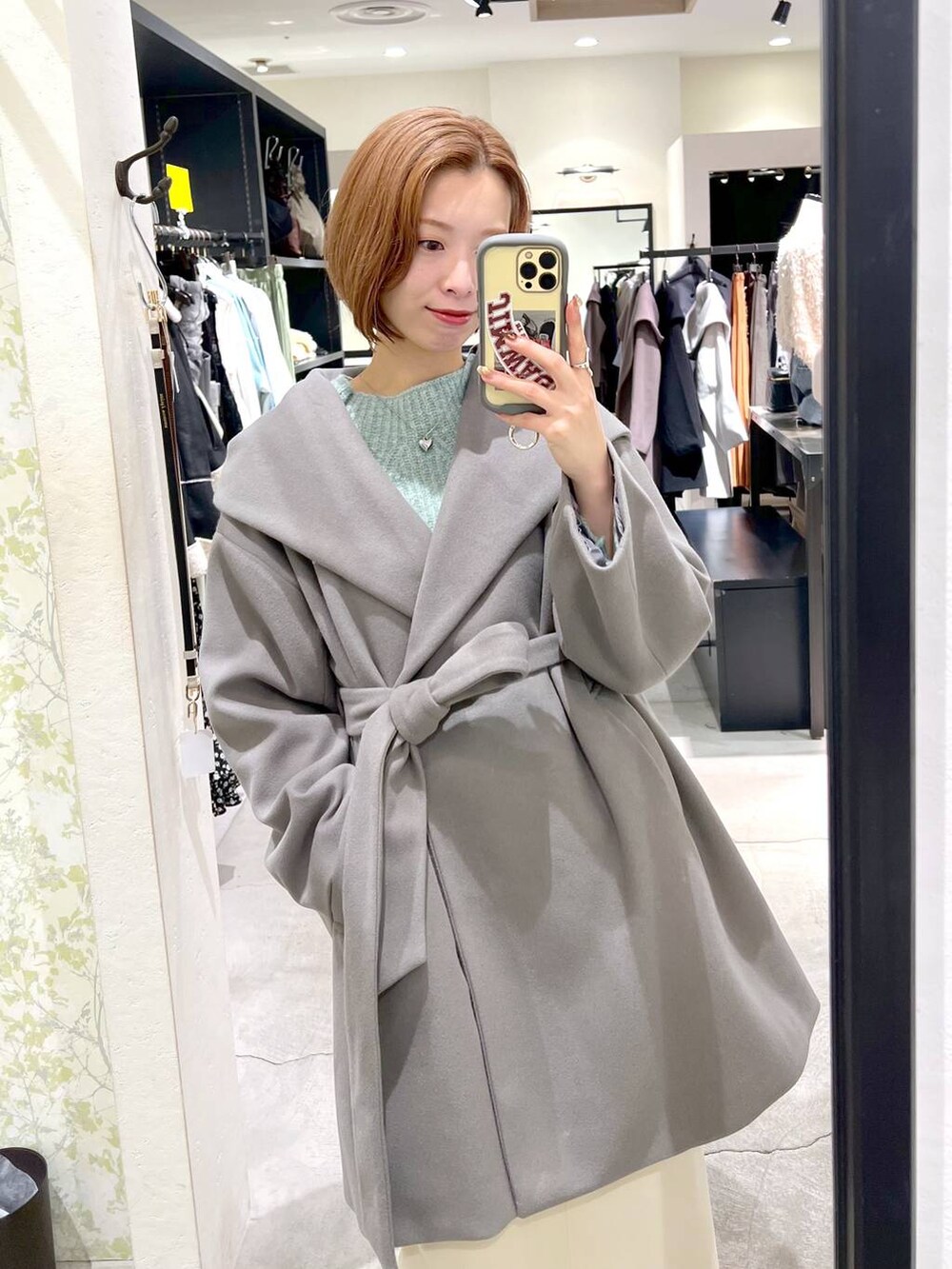 グレー系のノーカラーコート、ブラック系のショルダーバッグ、ブラック系のブーツを着用したレディースの秋コーディネートの5枚目の写真