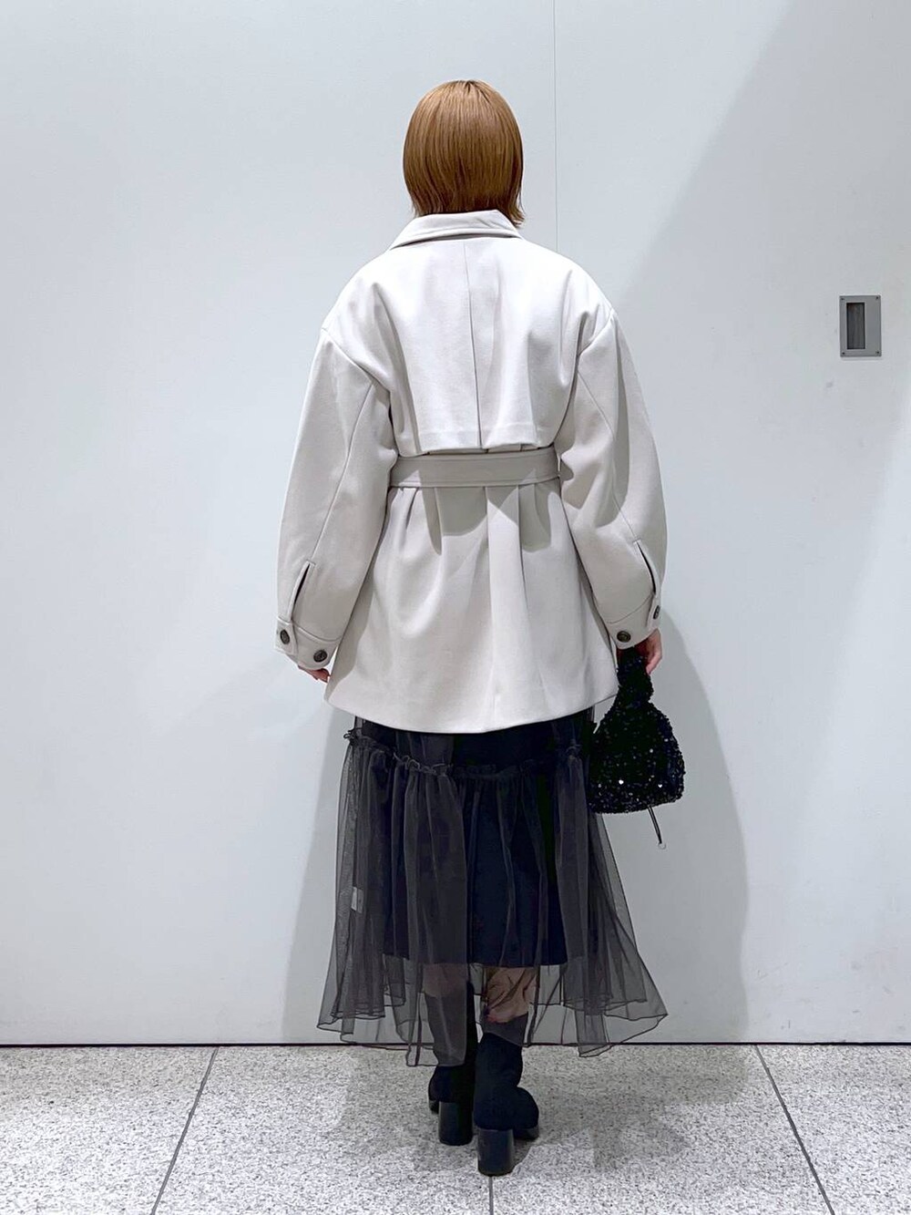 ホワイト系のチェスターコート、ブラック系のブーツ、ブラック系のハンドバッグを着用したレディースの冬コーディネートの3枚目の写真