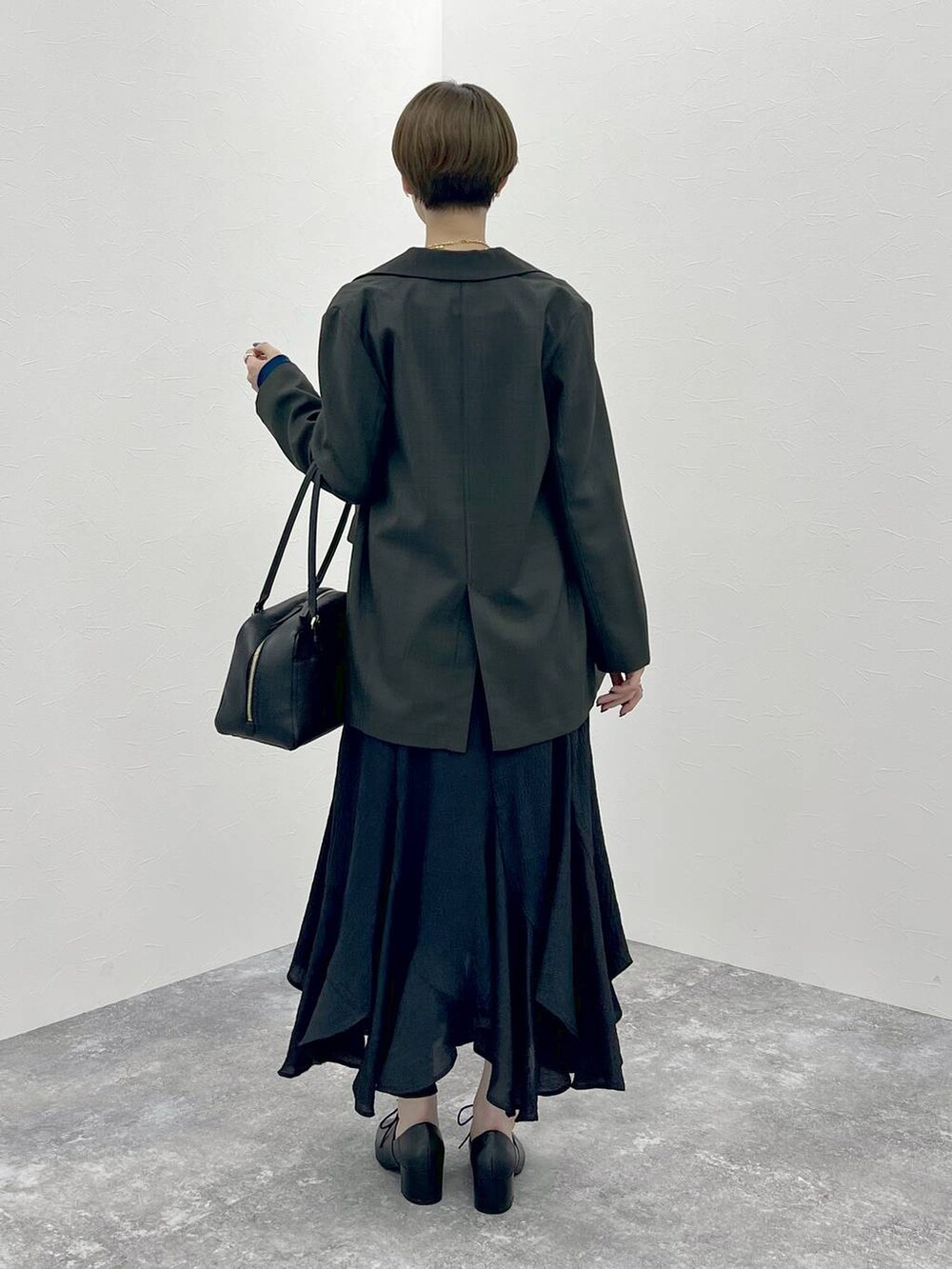 グレー系のテーラードジャケット、ブラック系のハンドバッグ、ブラック系のスカートを着用したレディースの秋コーディネートの3枚目の写真