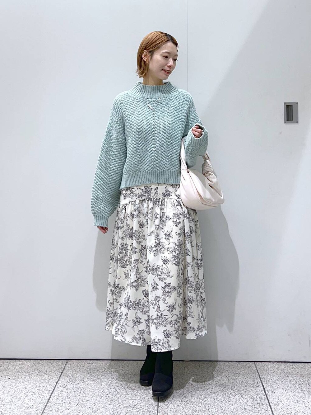 ブラック系のブーツ、ホワイト系のハンドバッグ、グリーン系のニット/セーターを着用したレディースの冬コーディネートの2枚目の写真