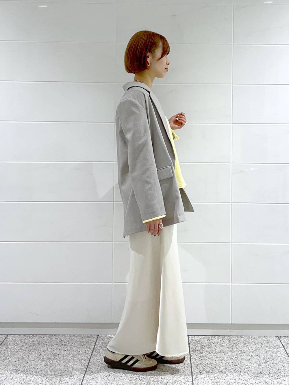 イエロー系のニット/セーター、グレー系のテーラードジャケット、ホワイト系のスカートを着用したレディースの春コーディネートの2枚目の写真