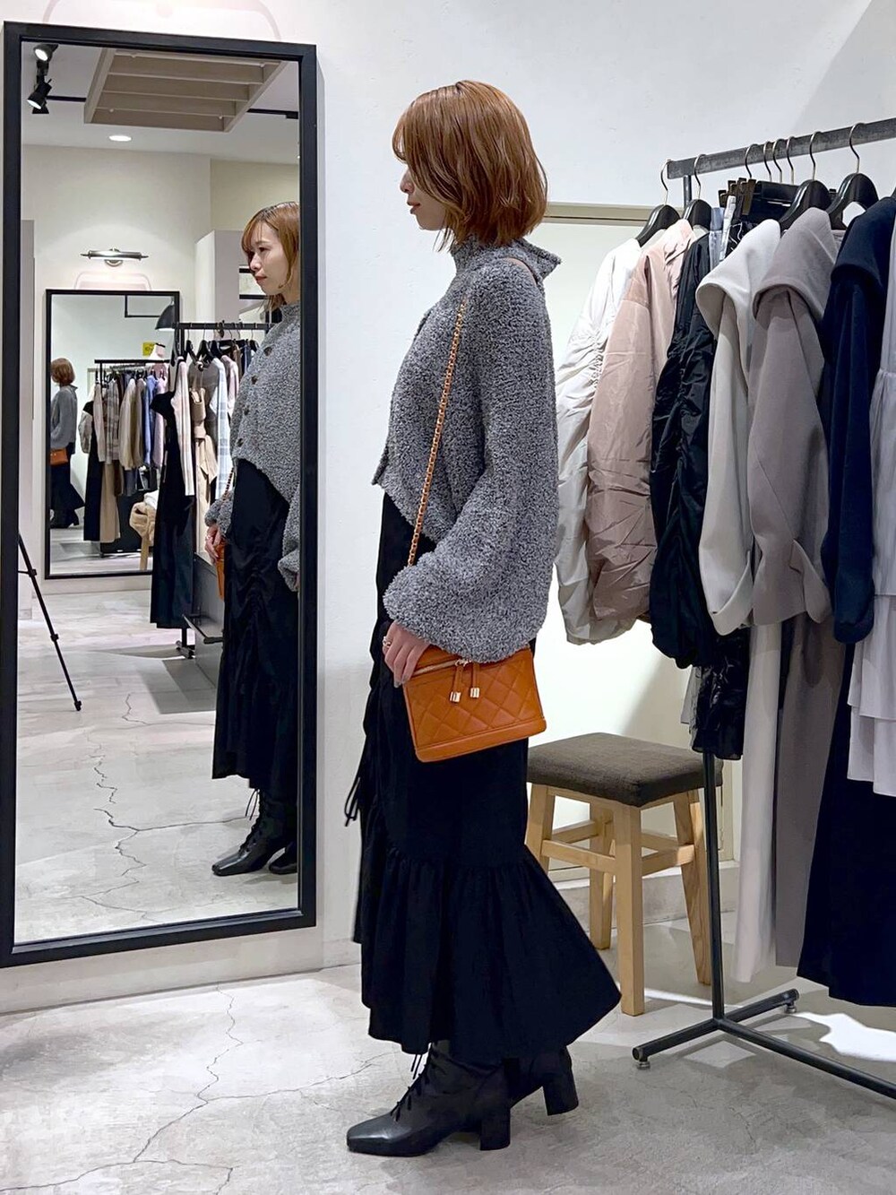 ブラック系のブーツ、オレンジ系のショルダーバッグ、ブラック系のスカートを着用したレディースの秋コーディネートの2枚目の写真