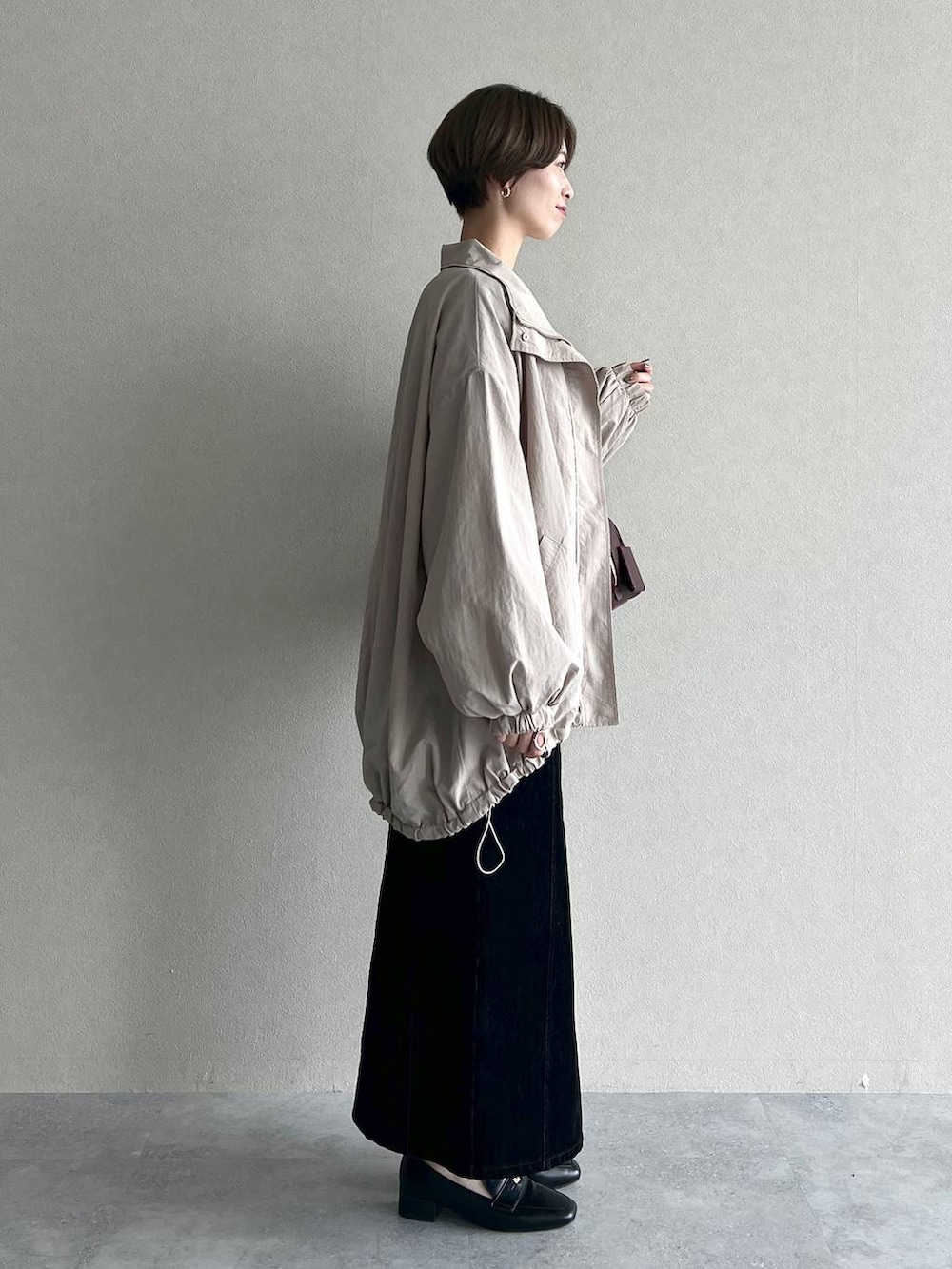 レッド系のハンドバッグ、ブラック系のスカート、ブラック系のローファーを着用したレディースの秋コーディネートの2枚目の写真