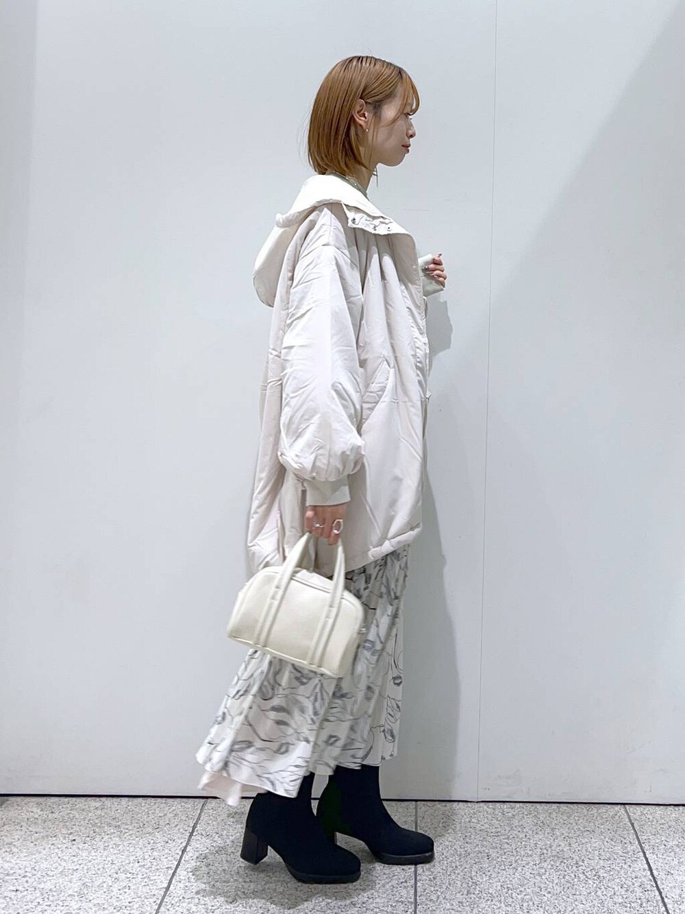 ホワイト系のブルゾン、ホワイト系のボストンバッグ、ブラック系のブーツを着用したレディースの秋コーディネートの2枚目の写真