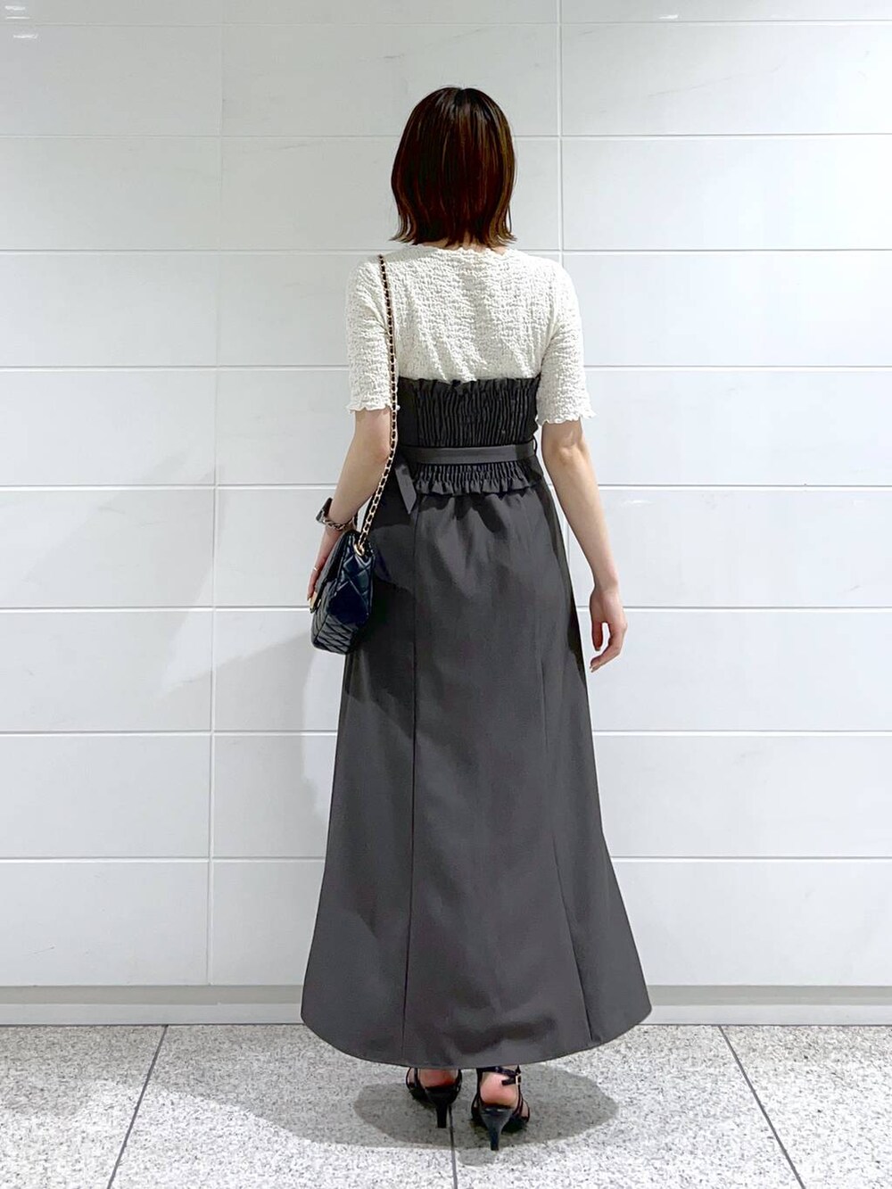 グレー系のスカート、ホワイト系のTシャツ/カットソー、ブラック系のショルダーバッグを着用したレディースの春コーディネートの4枚目の写真