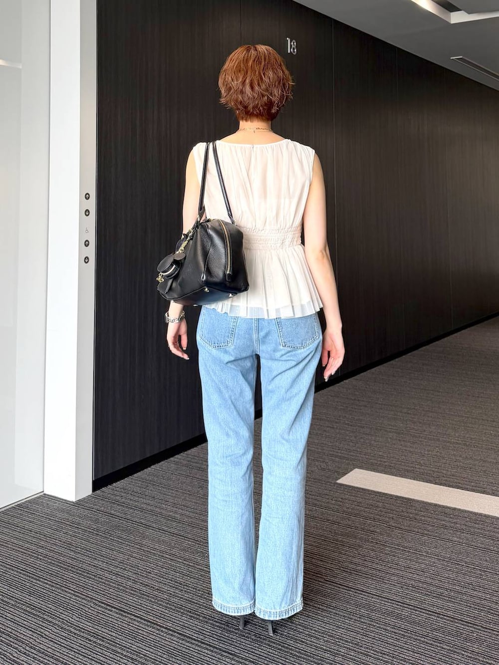 ブラック系のハンドバッグ、ブルー系のデニムパンツを着用したレディースの夏コーディネートの3枚目の写真