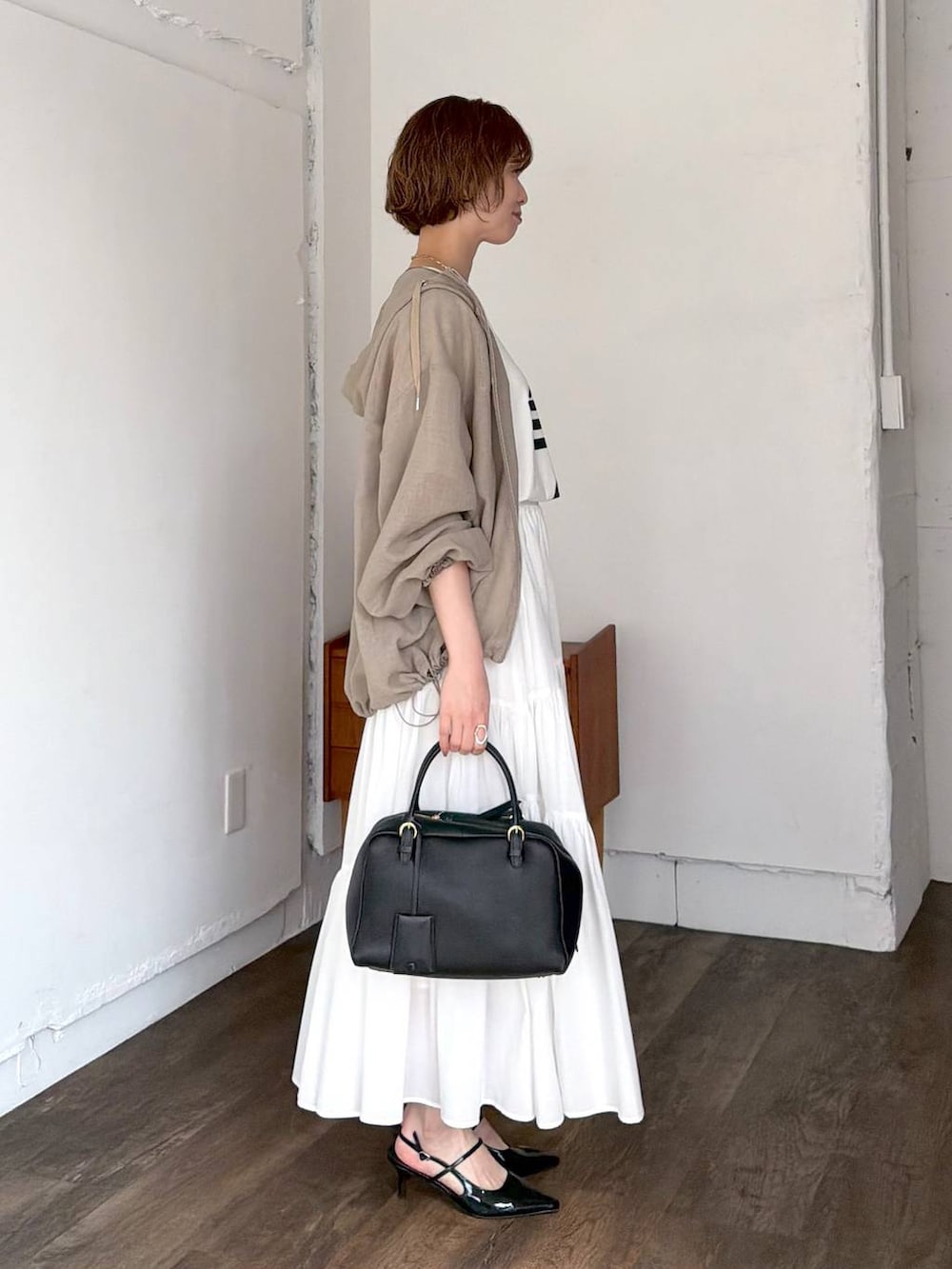 ブラック系のハンドバッグ、ブラック系のサンダル、ホワイト系のスカートを着用したレディースの春コーディネートの2枚目の写真