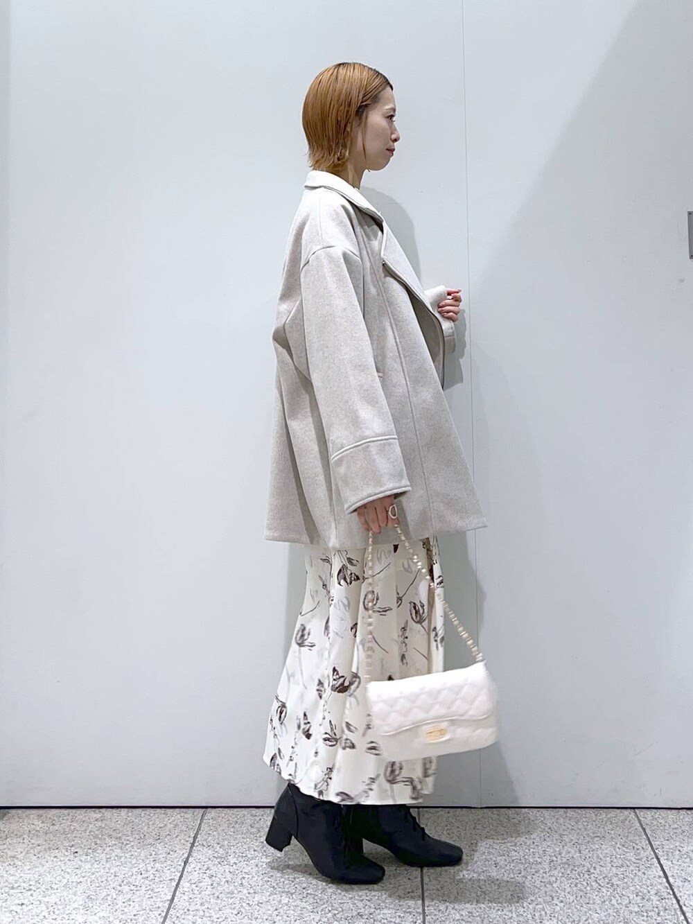 ホワイト系のショルダーバッグ、ブラック系のブーツ、ホワイト系のチェスターコートを着用したレディースの冬コーディネートの2枚目の写真