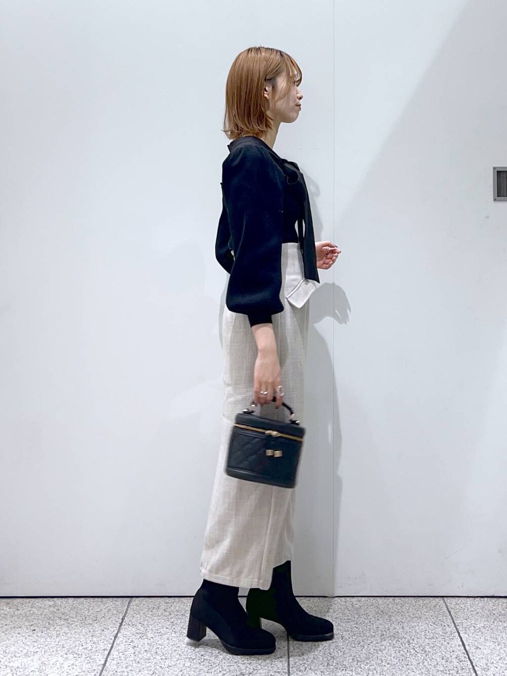 ブラック系のブーツ、ブラック系のショルダーバッグ、ホワイト系のスカートを着用したレディースの秋コーディネートの2枚目の写真