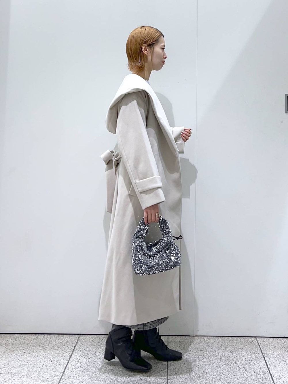 ブルー系のニット/セーター、ホワイト系のノーカラーコート、ブラック系のブーツを着用したレディースの冬コーディネートの2枚目の写真