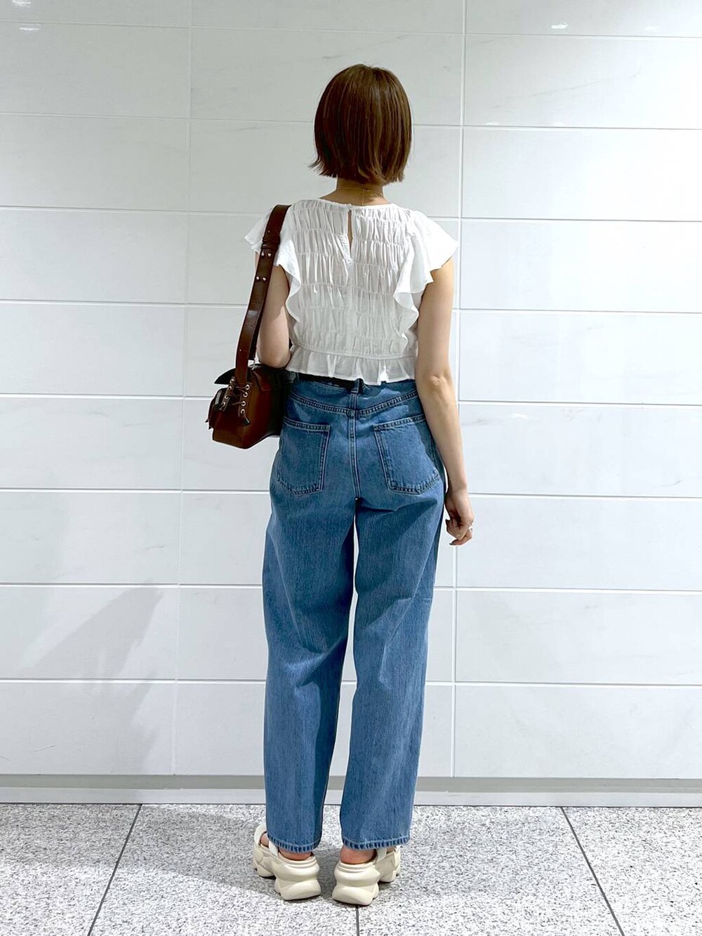 ブルー系のデニムパンツ、ホワイト系のサンダル、ブラウン系のショルダーバッグを着用したレディースの春コーディネートの4枚目の写真