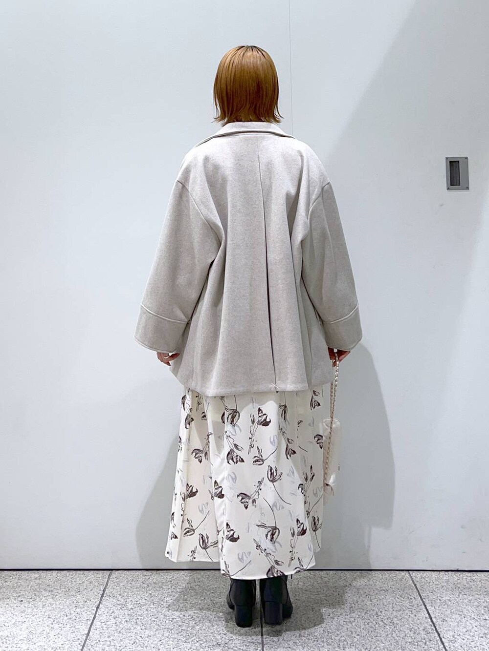 ホワイト系のショルダーバッグ、ブラック系のブーツ、ホワイト系のチェスターコートを着用したレディースの冬コーディネートの3枚目の写真