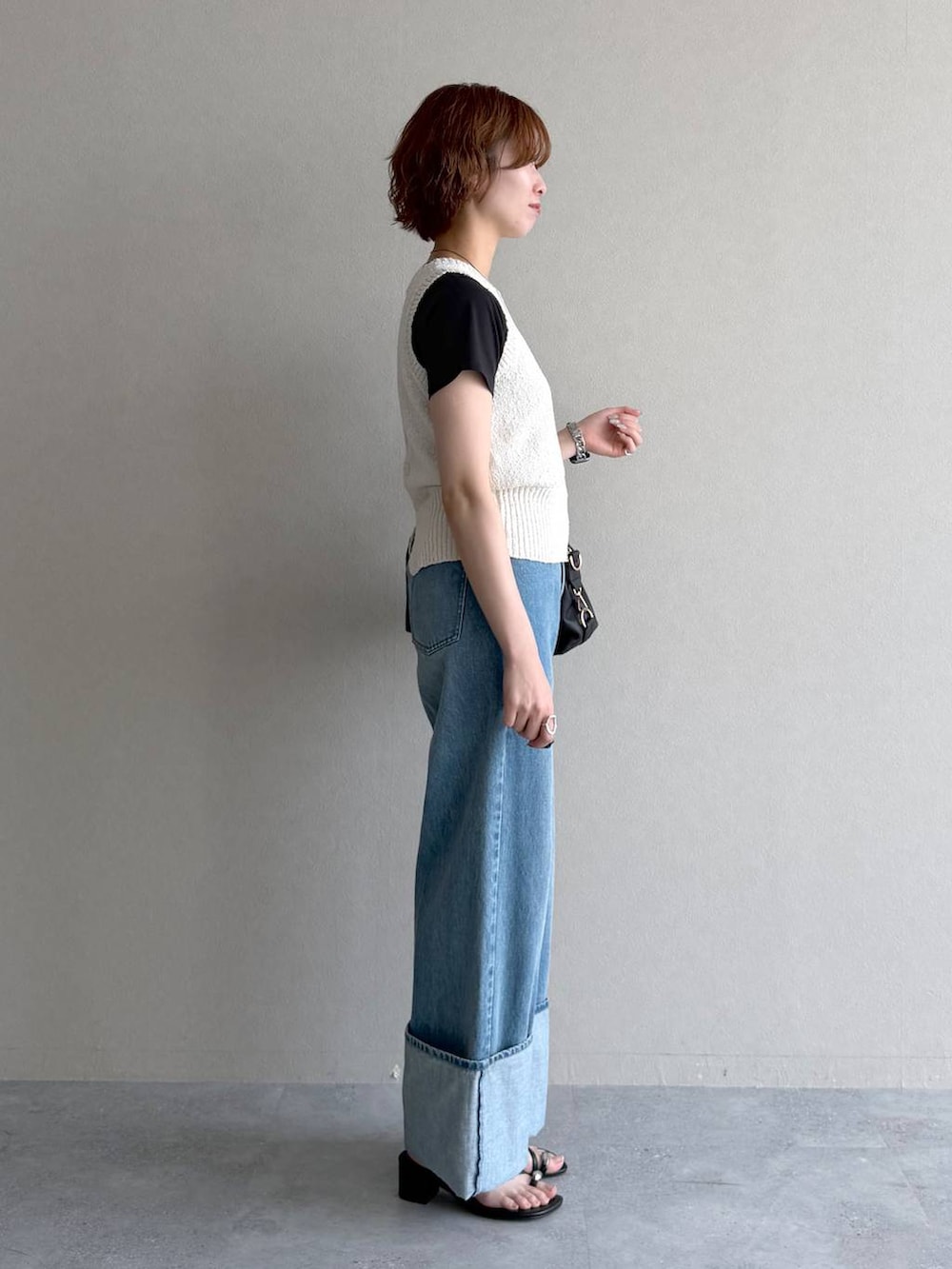 ブラック系のボストンバッグ、ブルー系のデニムパンツ、ホワイト系のベストを着用したレディースの夏コーディネートの2枚目の写真