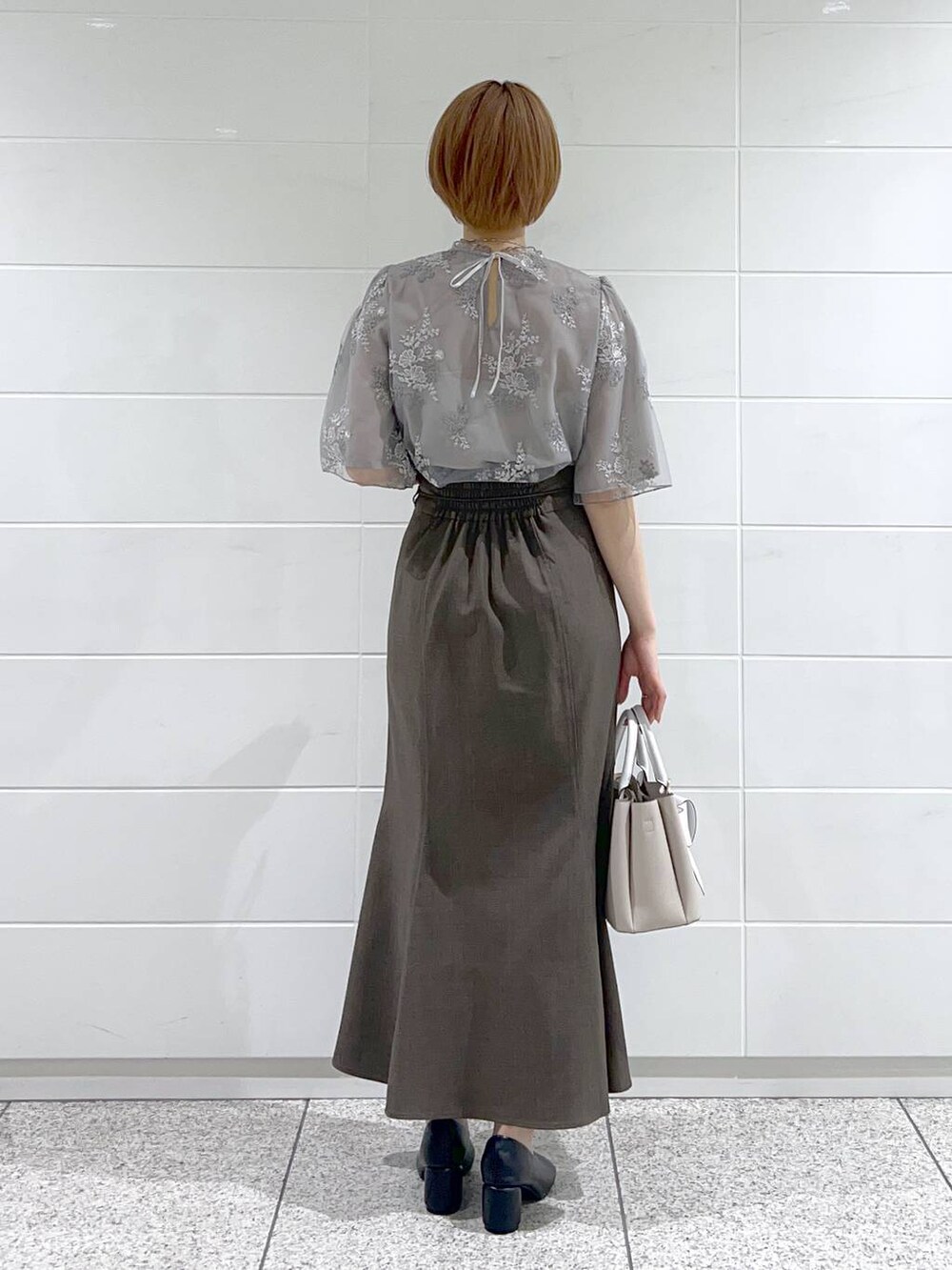 ベージュ系のショルダーバッグ、ブラック系のパンプス、グレー系のスカートを着用したレディースの春コーディネートの3枚目の写真