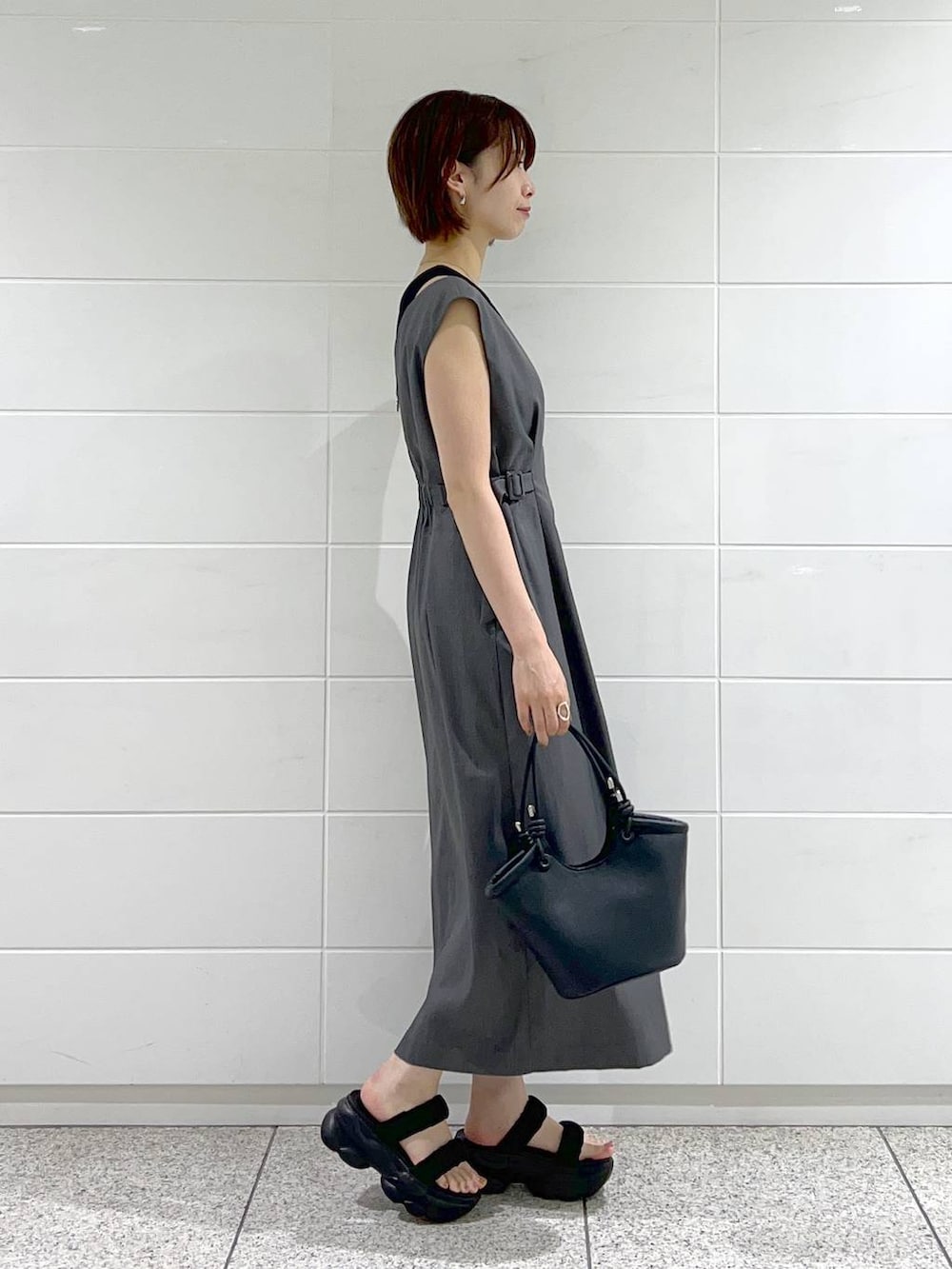 ブラック系のハンドバッグ、ブラック系のサンダル、グレー系のジャンパースカートを着用したレディースの夏コーディネートの2枚目の写真