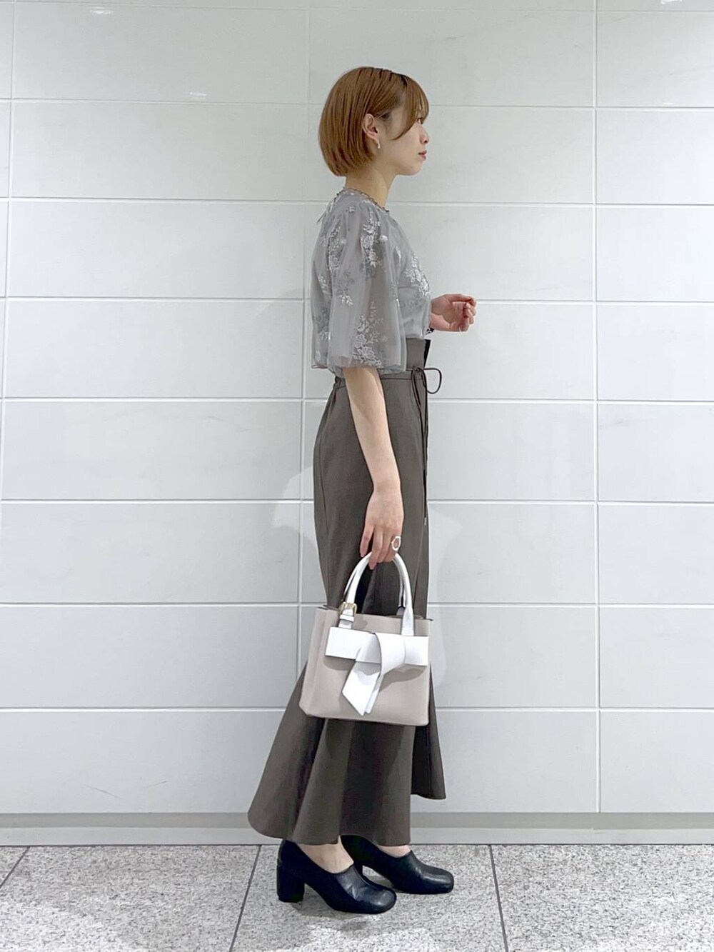 ベージュ系のショルダーバッグ、ブラック系のパンプス、グレー系のスカートを着用したレディースの春コーディネートの2枚目の写真