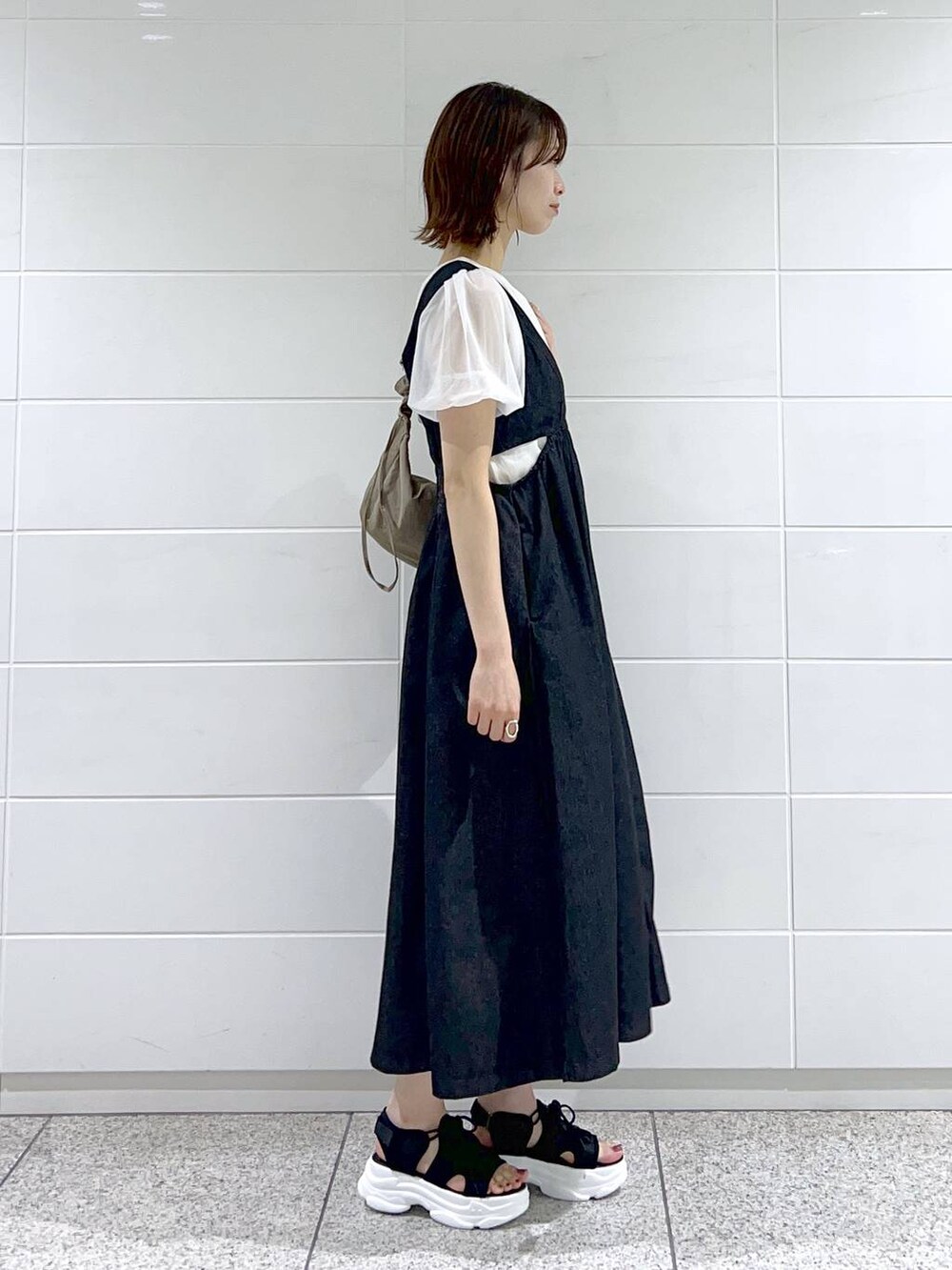 ブラック系のサンダル、ブラック系のジャンパースカート、ブラウン系のショルダーバッグを着用したレディースの春コーディネートの3枚目の写真