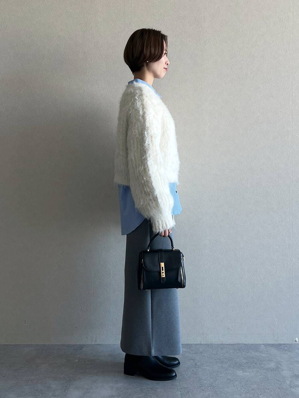 グレー系のスカート、ブラック系のブーツ、ホワイト系のニット/セーターを着用したレディースの冬コーディネートの2枚目の写真