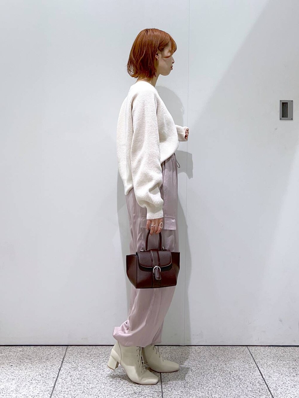 ホワイト系のニット/セーター、ブラウン系のハンドバッグ、ホワイト系のブーツを着用したレディースの秋コーディネートの2枚目の写真