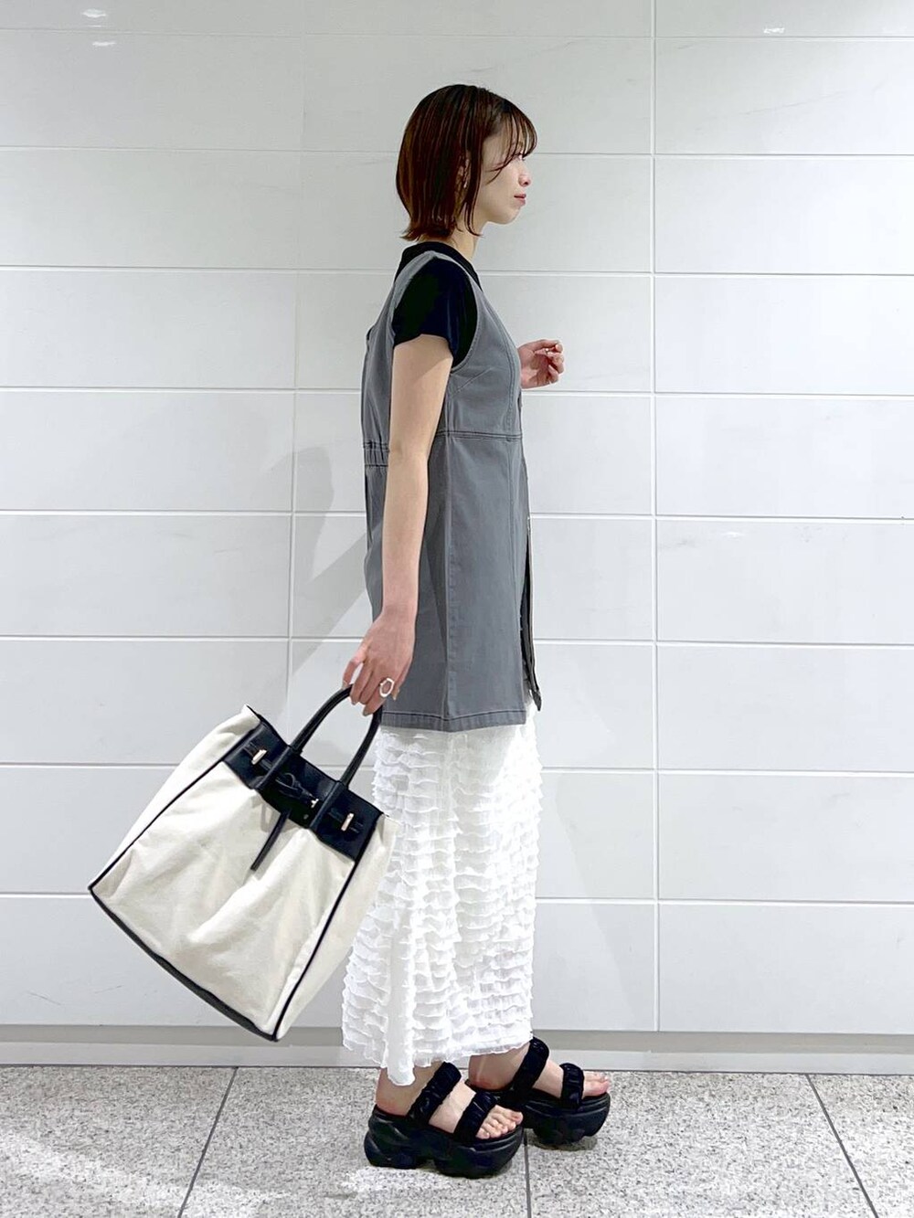 ブラック系のトートバッグ、ブラック系のTシャツ/カットソー、ブラック系のサンダルを着用したレディースの春コーディネートの3枚目の写真