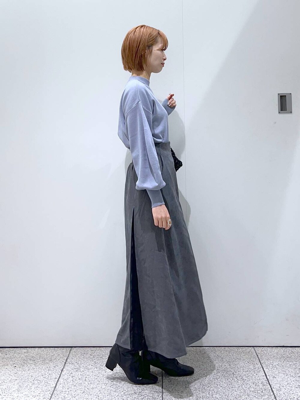 ブラック系のブーツ、ブルー系のニット/セーター、ブラック系のハンドバッグを着用したレディースの冬コーディネートの2枚目の写真