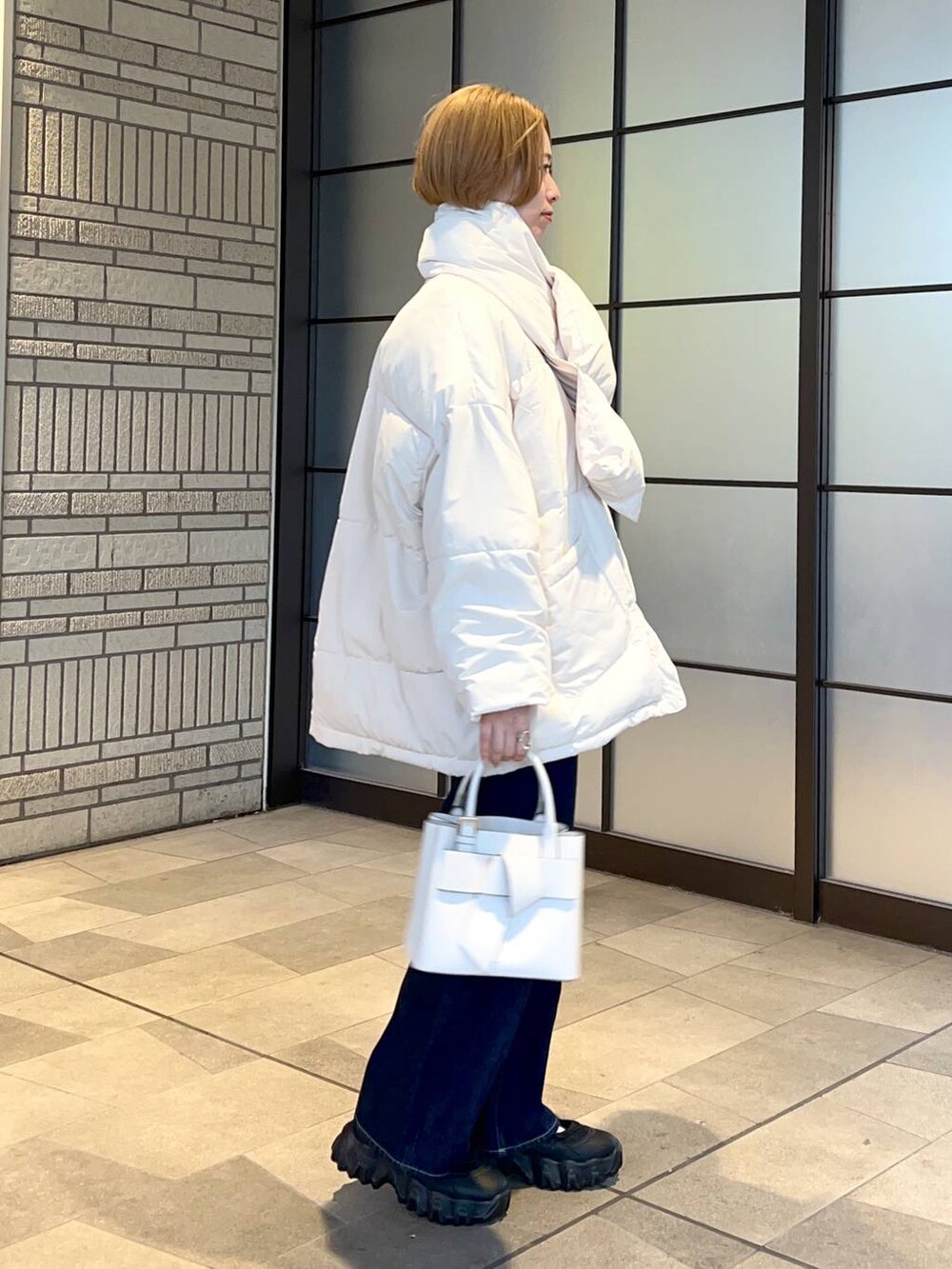 ホワイト系のブルゾン、ホワイト系のショルダーバッグ、ブルー系のスラックスを着用したレディースの冬コーディネートの2枚目の写真