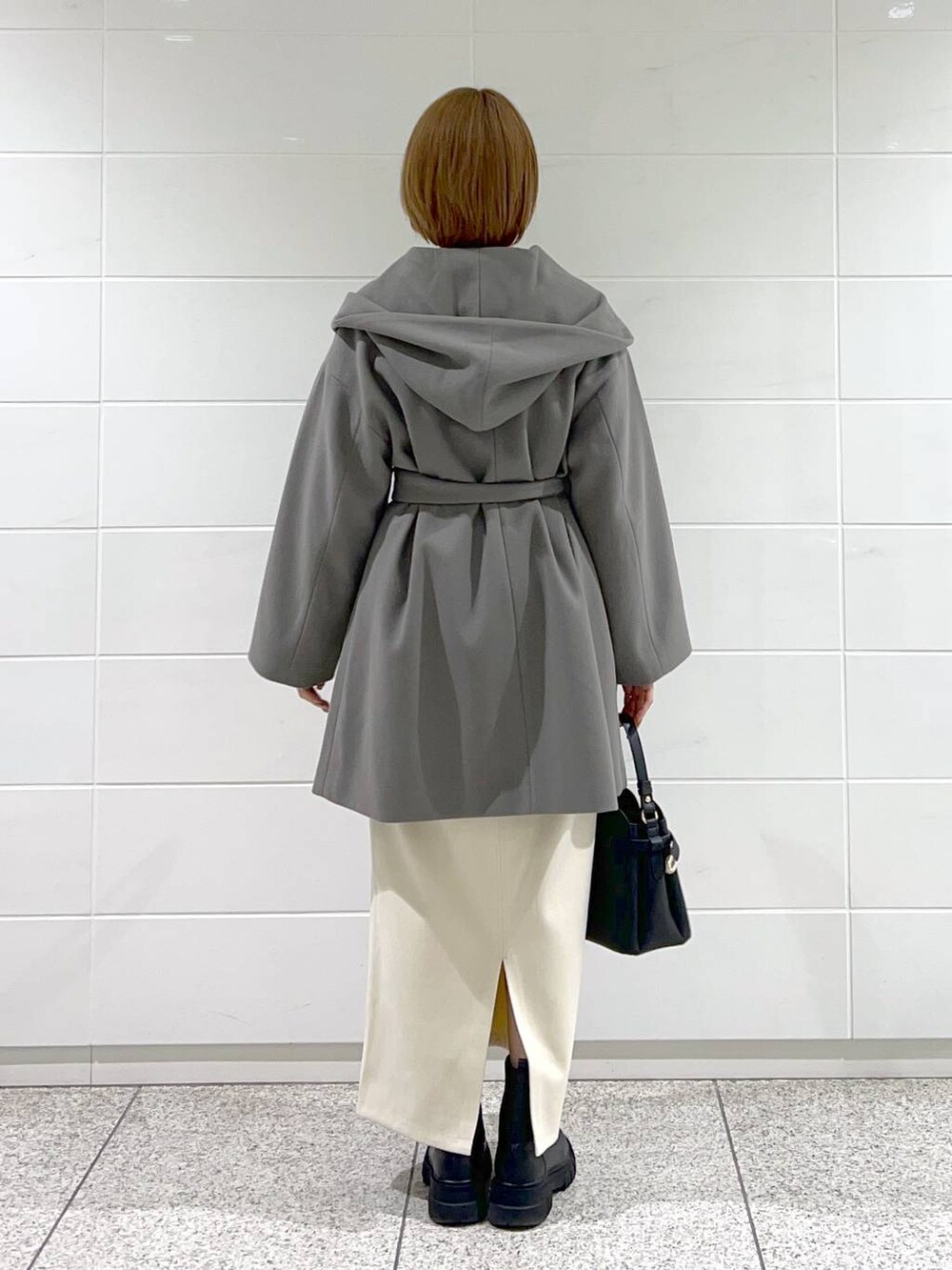 グレー系のノーカラーコート、ブラック系のショルダーバッグ、ブラック系のブーツを着用したレディースの秋コーディネートの3枚目の写真